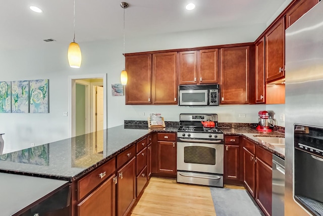 kitchen featuring dark stone countertops, stainless steel appliances, a peninsula, light wood finished floors, and hanging light fixtures