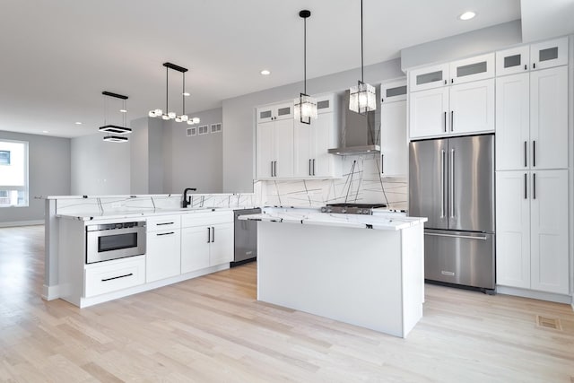 kitchen featuring a center island, stainless steel appliances, decorative backsplash, a peninsula, and wall chimney exhaust hood