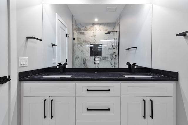 full bathroom featuring double vanity, a marble finish shower, and a sink