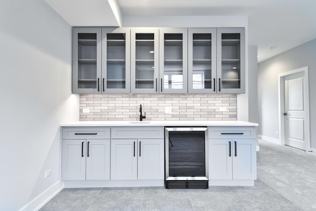 bar with beverage cooler, tasteful backsplash, a sink, and baseboards