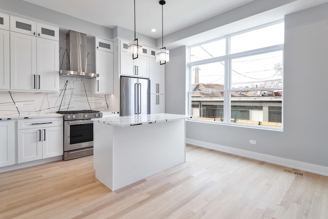 kitchen featuring appliances with stainless steel finishes, a center island, light wood-type flooring, wall chimney range hood, and backsplash