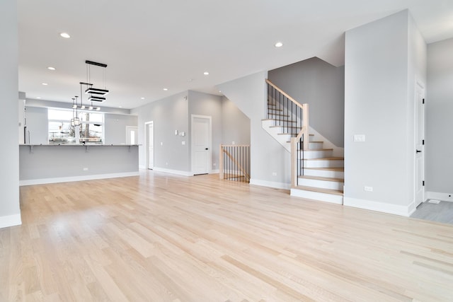 unfurnished living room featuring light wood-type flooring, stairs, baseboards, and recessed lighting