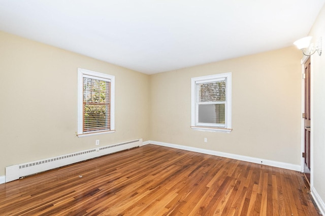 empty room featuring a baseboard heating unit, baseboards, and wood finished floors