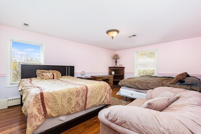 bedroom with a baseboard radiator, wood finished floors, and visible vents