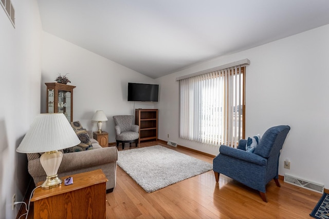 living area featuring vaulted ceiling, baseboards, visible vents, and light wood-style floors