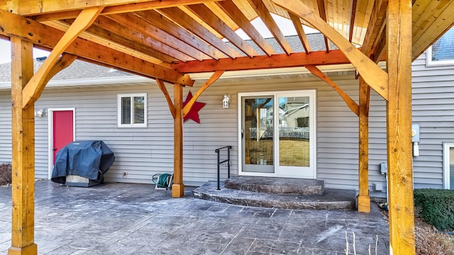 view of exterior entry featuring a patio area and a shingled roof