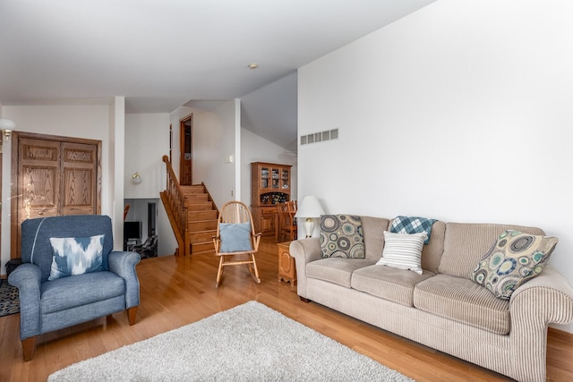 living room with lofted ceiling, visible vents, stairway, and wood finished floors