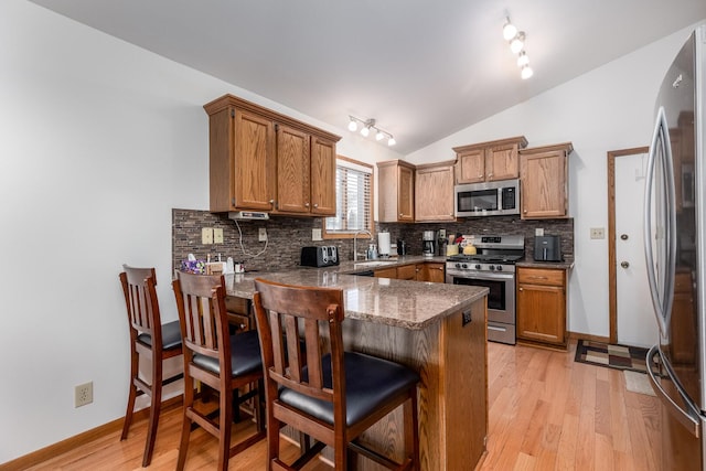 kitchen featuring light wood finished floors, tasteful backsplash, appliances with stainless steel finishes, a peninsula, and vaulted ceiling