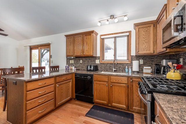 kitchen featuring stainless steel appliances, a peninsula, a sink, light wood-type flooring, and backsplash