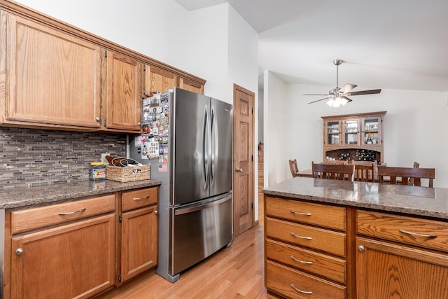 kitchen featuring light wood-style flooring, dark stone countertops, freestanding refrigerator, and decorative backsplash