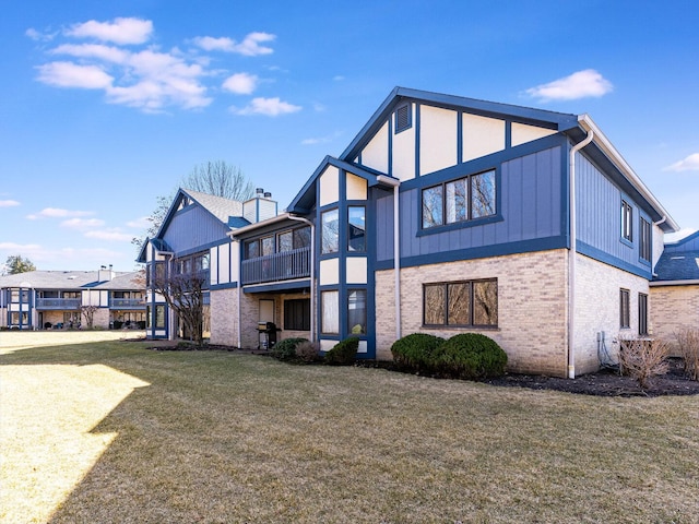 rear view of house featuring a yard, brick siding, and a balcony