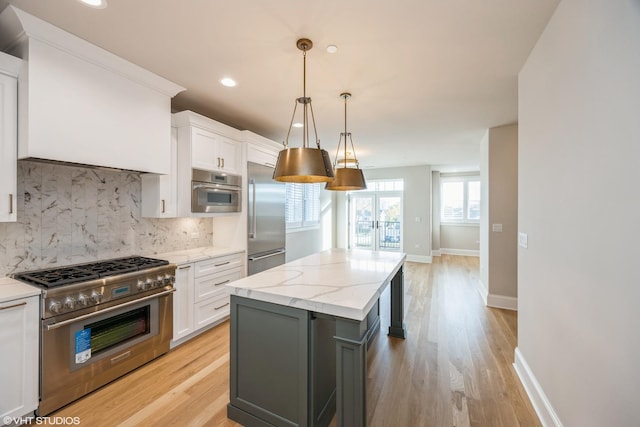 kitchen featuring high end appliances, white cabinetry, light wood-style flooring, and tasteful backsplash