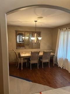 dining area featuring arched walkways, a notable chandelier, and wood finished floors