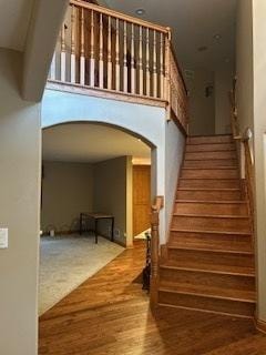 stairway featuring arched walkways and wood finished floors