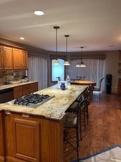 kitchen featuring brown cabinetry, stainless steel gas cooktop, pendant lighting, light stone counters, and dark wood-style floors