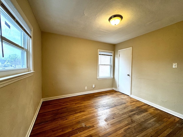 unfurnished room with a textured ceiling, baseboards, and wood finished floors