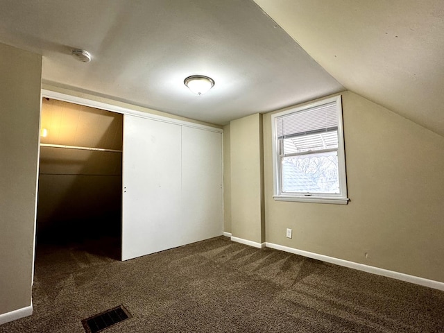 unfurnished bedroom featuring dark colored carpet, a closet, visible vents, vaulted ceiling, and baseboards