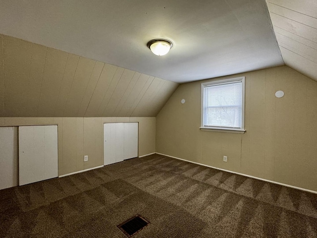 additional living space with dark colored carpet, visible vents, and vaulted ceiling