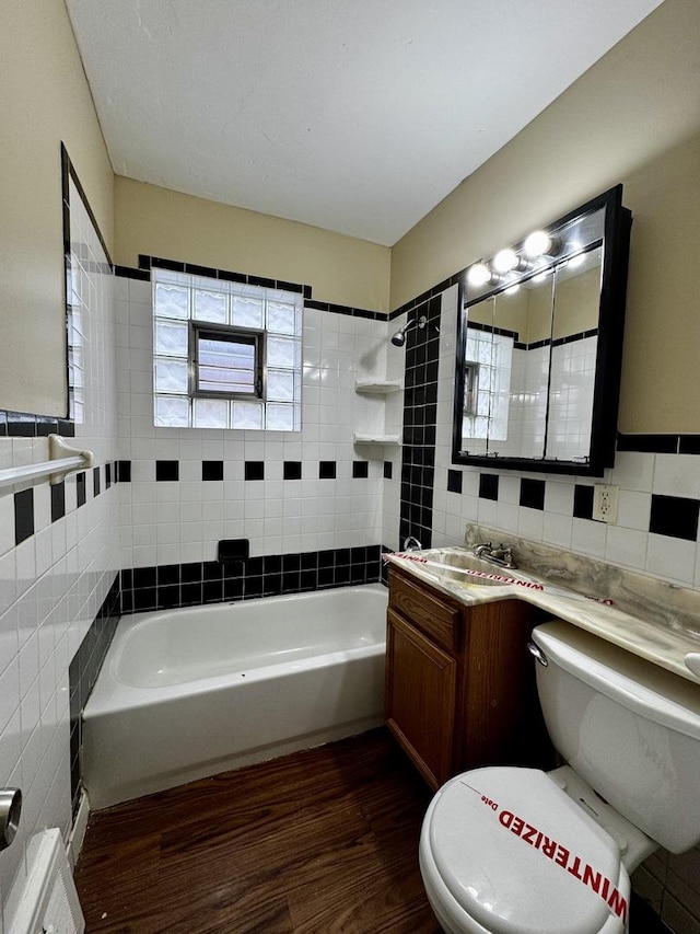 full bath featuring toilet, shower / bath combination, wood finished floors, vanity, and tile walls