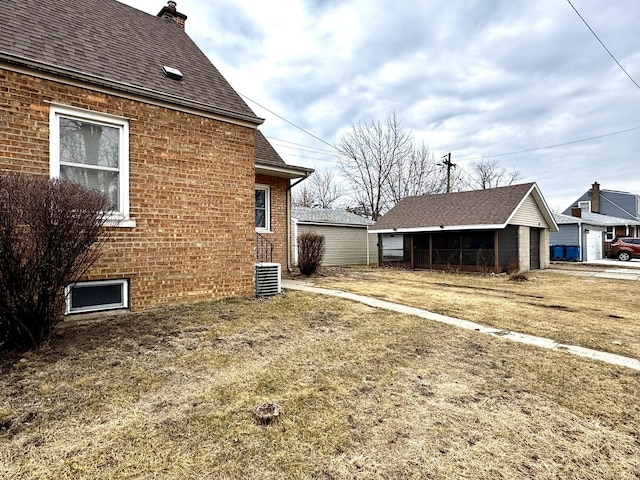 view of property exterior featuring an outbuilding, brick siding, a chimney, and roof with shingles