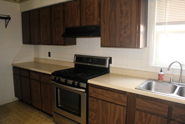 kitchen featuring under cabinet range hood, a sink, gas stove, light countertops, and dark brown cabinets