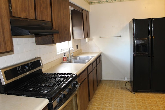 kitchen featuring a sink, light countertops, under cabinet range hood, gas range, and black fridge