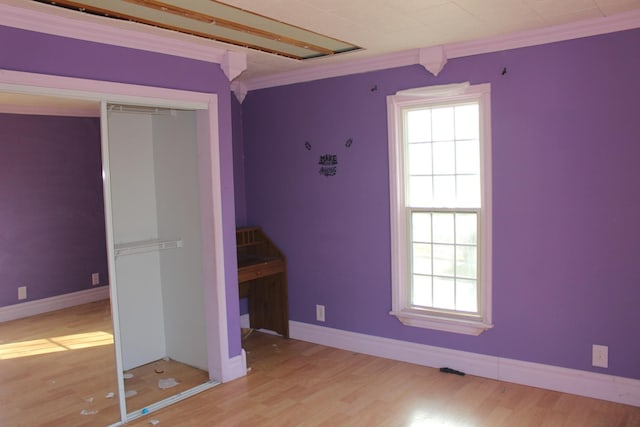 unfurnished bedroom featuring crown molding, multiple windows, wood finished floors, and a closet