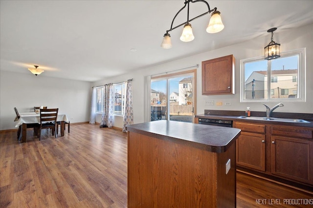 kitchen featuring dark wood finished floors, dark countertops, a healthy amount of sunlight, a kitchen island, and a sink