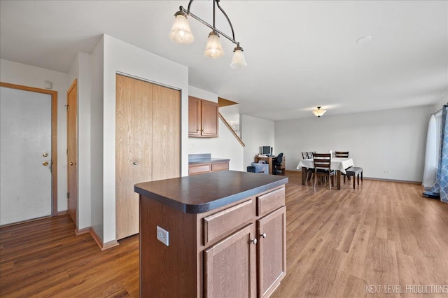 kitchen featuring baseboards, dark countertops, a kitchen island, decorative light fixtures, and light wood-type flooring