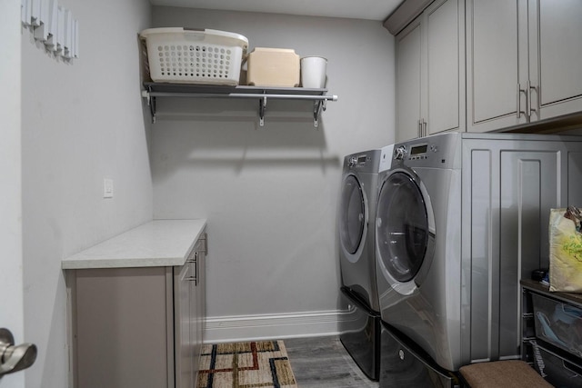 clothes washing area with cabinet space, washer and dryer, baseboards, and wood finished floors