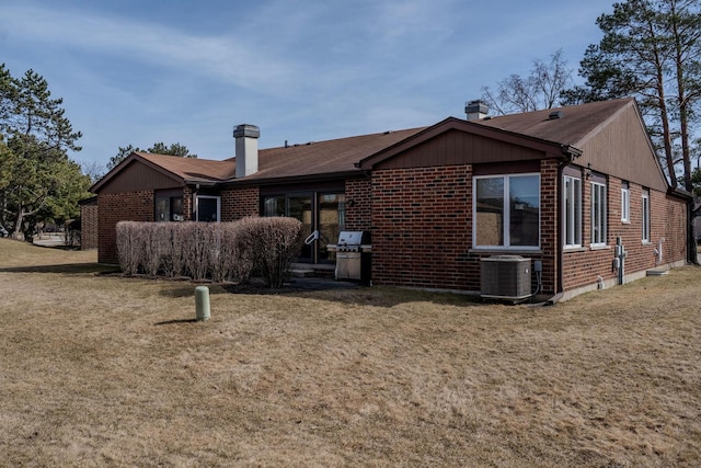 back of house featuring a lawn, central AC unit, brick siding, and a chimney