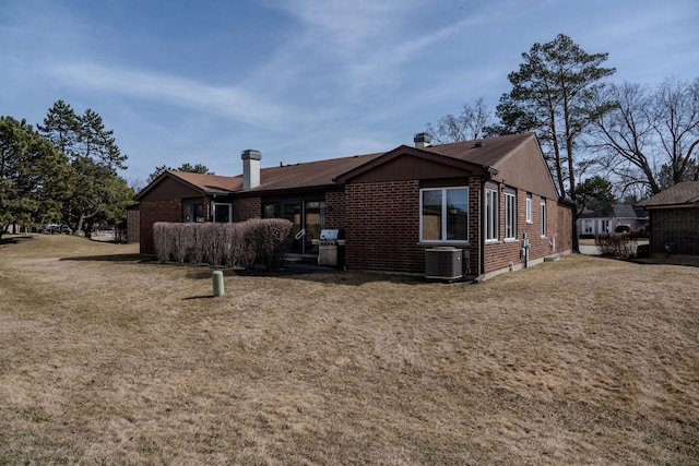 rear view of house featuring central air condition unit, brick siding, and a lawn