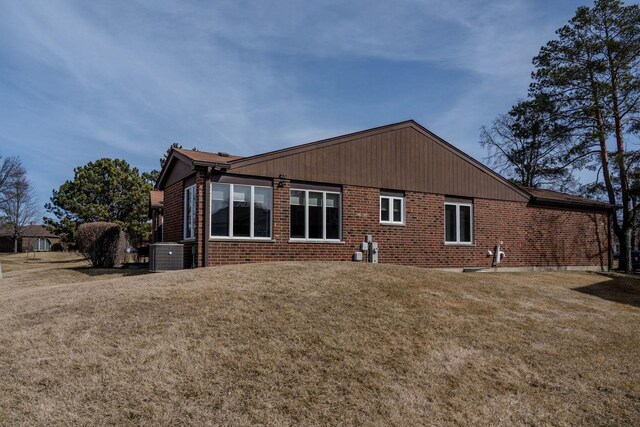 rear view of property featuring brick siding, central air condition unit, and a yard