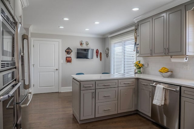 kitchen featuring light countertops, ornamental molding, gray cabinets, appliances with stainless steel finishes, and a peninsula