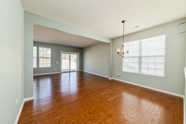 empty room with a chandelier, visible vents, baseboards, and dark wood-style floors