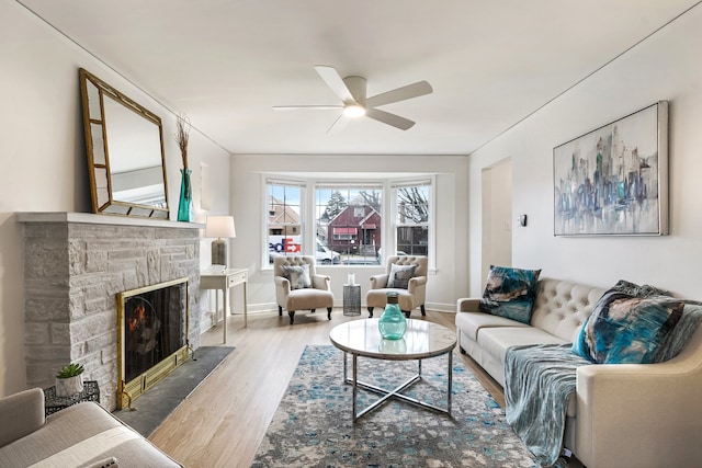 living area featuring ceiling fan, a fireplace, baseboards, and wood finished floors