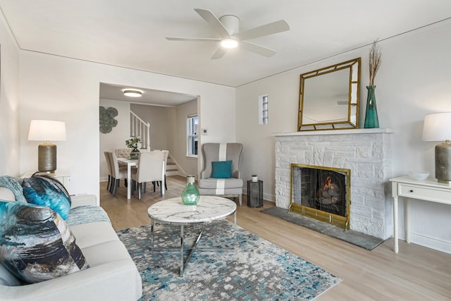 living room featuring baseboards, a ceiling fan, stairway, wood finished floors, and a stone fireplace