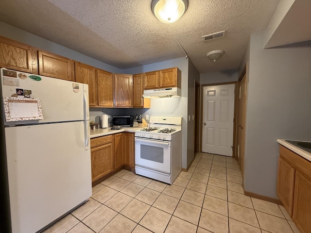 kitchen featuring light tile patterned flooring, under cabinet range hood, white appliances, visible vents, and light countertops