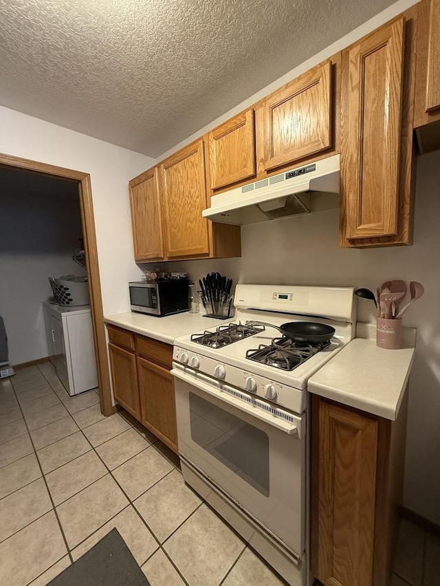 kitchen featuring white gas range oven, stainless steel microwave, brown cabinets, light countertops, and under cabinet range hood