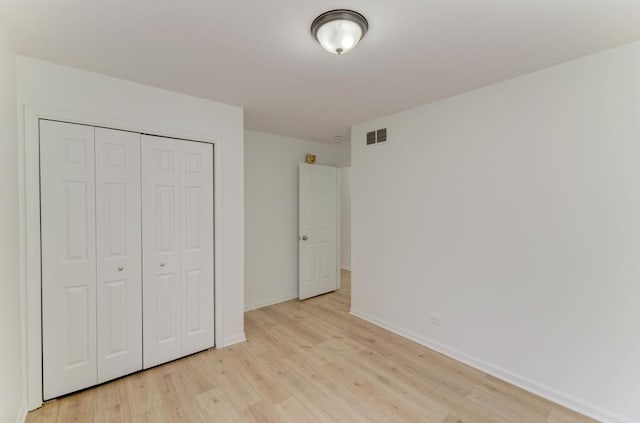 unfurnished bedroom with light wood-style floors, baseboards, visible vents, and a closet