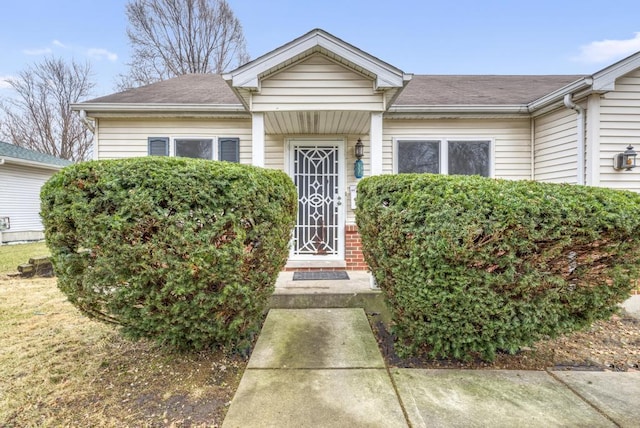 view of exterior entry featuring a shingled roof and brick siding