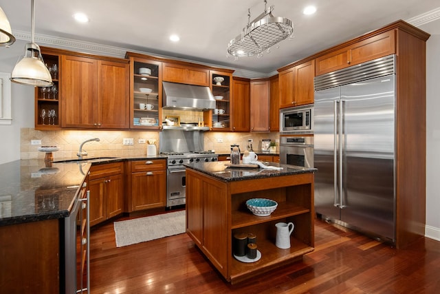 kitchen with open shelves, brown cabinetry, a sink, built in appliances, and under cabinet range hood