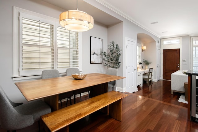 dining room with arched walkways, crown molding, baseboards, and wood finished floors