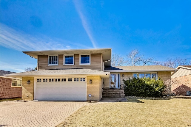 tri-level home featuring a garage, brick siding, decorative driveway, and a front yard