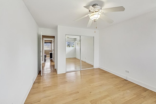 unfurnished bedroom featuring light wood-style floors, a ceiling fan, baseboards, and a closet