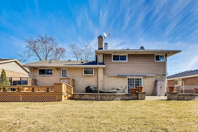 back of property featuring brick siding, a lawn, a wooden deck, a chimney, and a patio area