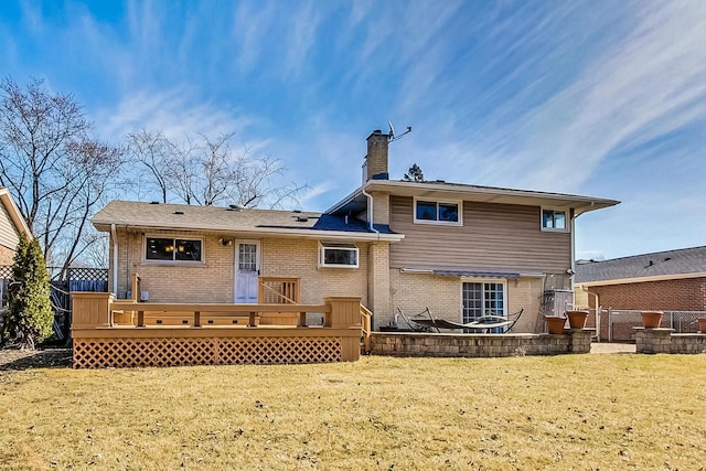 back of property featuring a chimney, fence, a deck, a yard, and brick siding