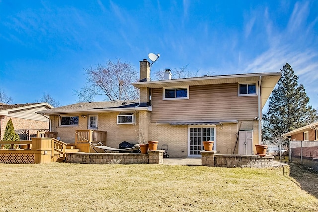 rear view of property featuring brick siding, a chimney, a lawn, fence, and a deck