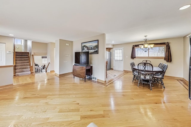 dining area featuring a notable chandelier, visible vents, baseboards, stairway, and light wood-type flooring