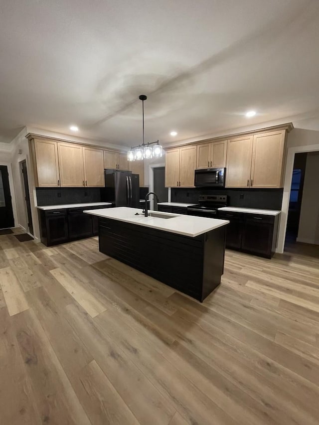 kitchen featuring black appliances, an island with sink, a sink, and light wood-style floors